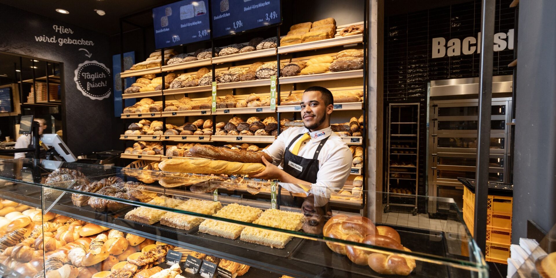 Mitarbeiter steht an Theke mit Brötchen und Brot